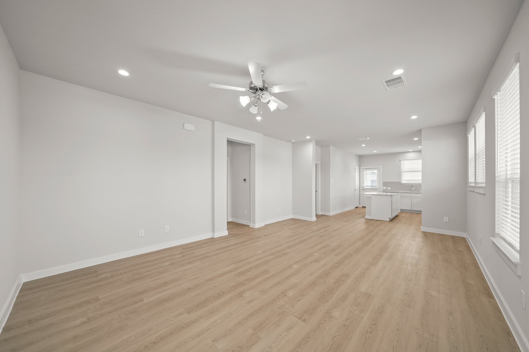 A large empty room with a ceiling fan and a wood floor.