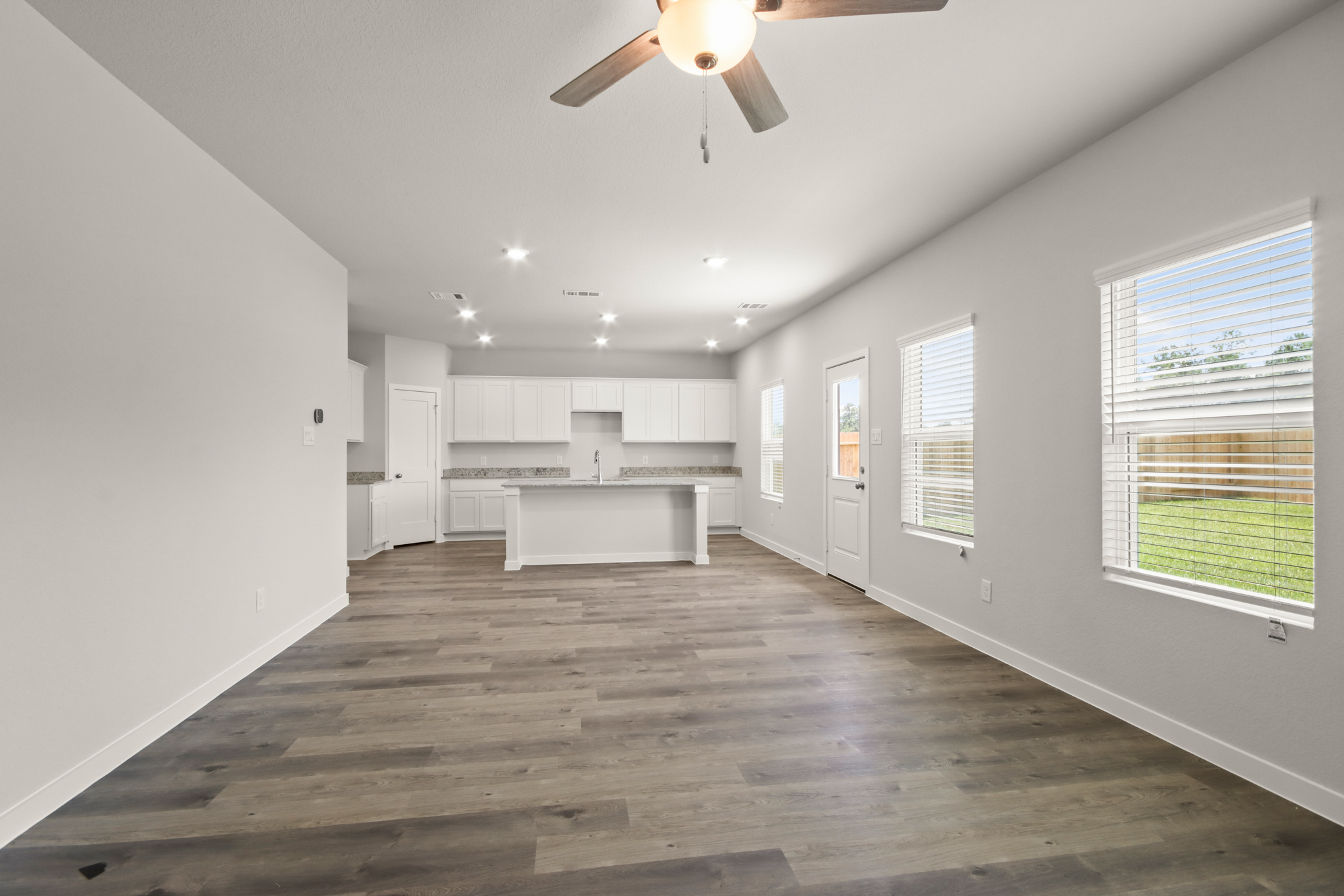 A large empty room with a ceiling fan and a wood floor.